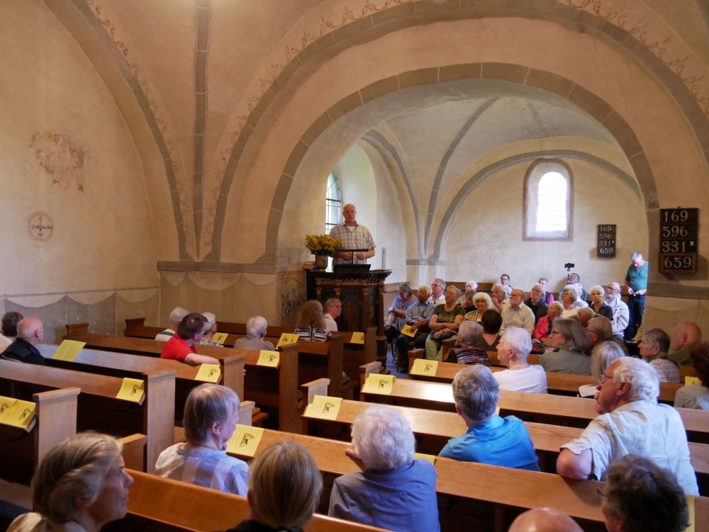 Orgelsommer in Donop - Kirchenführung mit Dirk Niederhöfer in der alten romanischen Kirche Donop. Kirche mit vielen Menschen in Bänken und Mann auf der Kanzel.